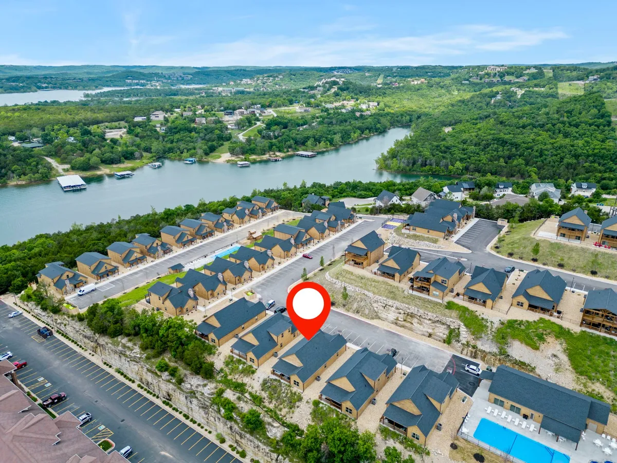 A sweeping exterior view features a row of inviting homes with a sparkling swimming pool in the foreground, lush greenery around the property, and a serene lake visible in the distance. The scene is bathed in warm sunlight, suggesting both relaxation and vibrant outdoor activity.