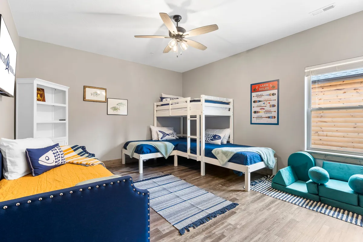 A cheerful bunkroom outfitted with built-in bunk beds, a colorful couch, and a generous bookshelf. The lively space is designed for both sleep and play, offering children and teens a cozy spot for bedtime stories, games, and fun hangouts.