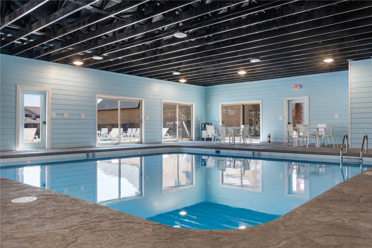 A bright, inviting indoor swimming pool is featured, bathed in natural light from large windows and surrounded by soft blue walls and comfortable seating areas. The tranquil atmosphere is ideal for year-round family fun, regardless of the weather outside.