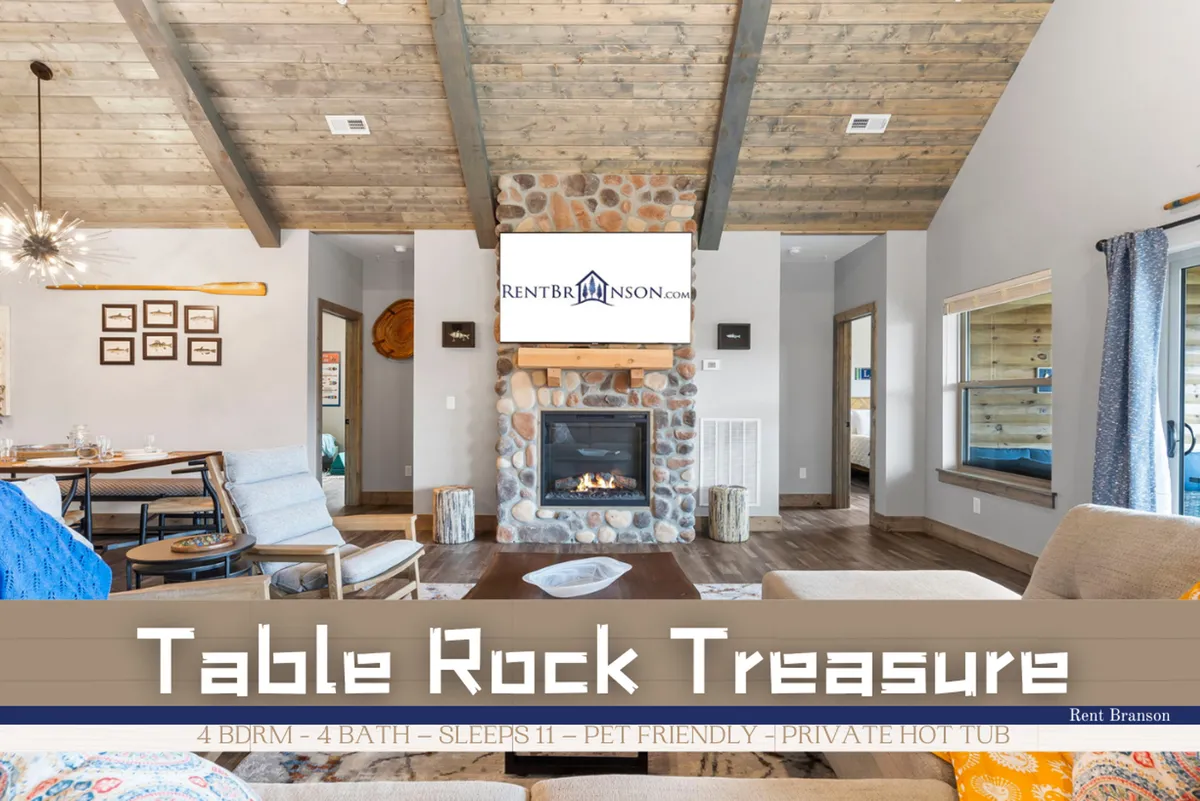 A spacious, open-concept interior featuring a stone fireplace as the focal point. The scene includes a large dining area and expansive windows that let natural light flood the space. Comfortable seating and a wall-mounted TV invite gatherings for games, movies, or conversation.