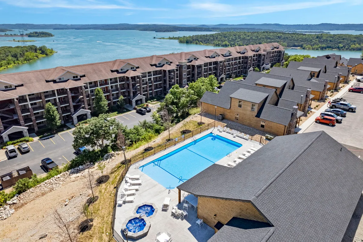 This exterior shot showcases a swimming pool and hot tub overlooking Table Rock Lake, with the backdrop of leafy trees and a relaxed apartment complex. The amenities are designed for both summer and year-round enjoyment, offering spaces for swimming, soaking, and outdoor gatherings.