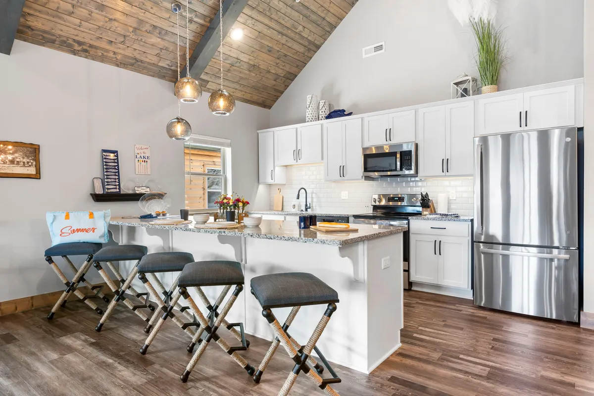 A stylish kitchen with a granite-topped island bar offering seating, stainless steel appliances, pendant lights, and exposed wooden beams. The scene is set for casual dining, meal prep, or simply enjoying company in a welcoming space.