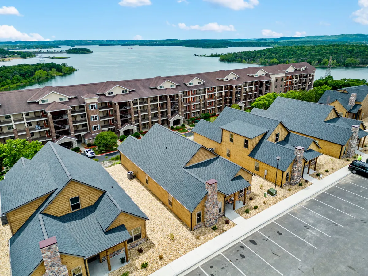 A picturesque lakefront scene featuring a mix of modern apartment buildings and charming cabins, with the tranquil waters of Table Rock Lake and surrounding greenery providing a serene backdrop. This is an inviting space for outdoor gatherings, relaxing by the water, or setting out on lake adventures.